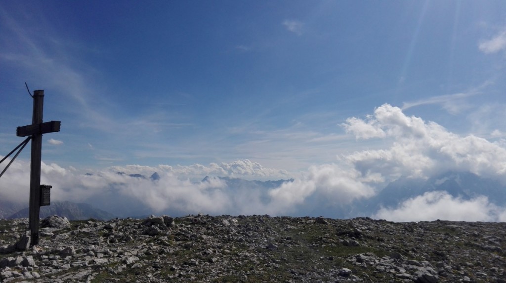Das Gipfelkreuz am Hohen Brett beobachtet die Wolkenspiele über den Berchtesgadener Alpen